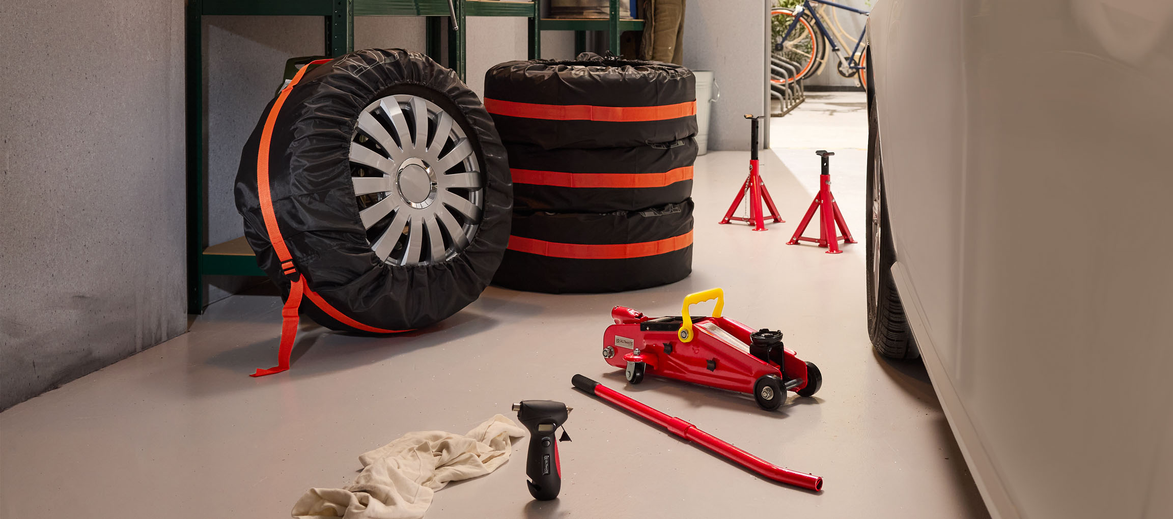 Automobilio padangos su užvalkalais, domkratas ir atramos garaže.