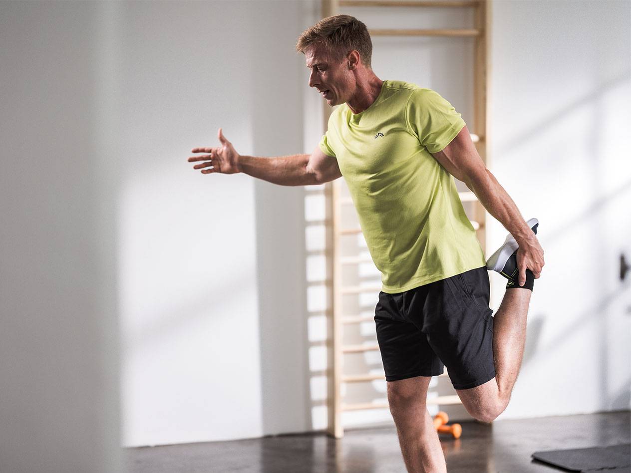 Vyras sporto salėje tempiasi su juodais šortais ir žalios spalvos marškinėliais.