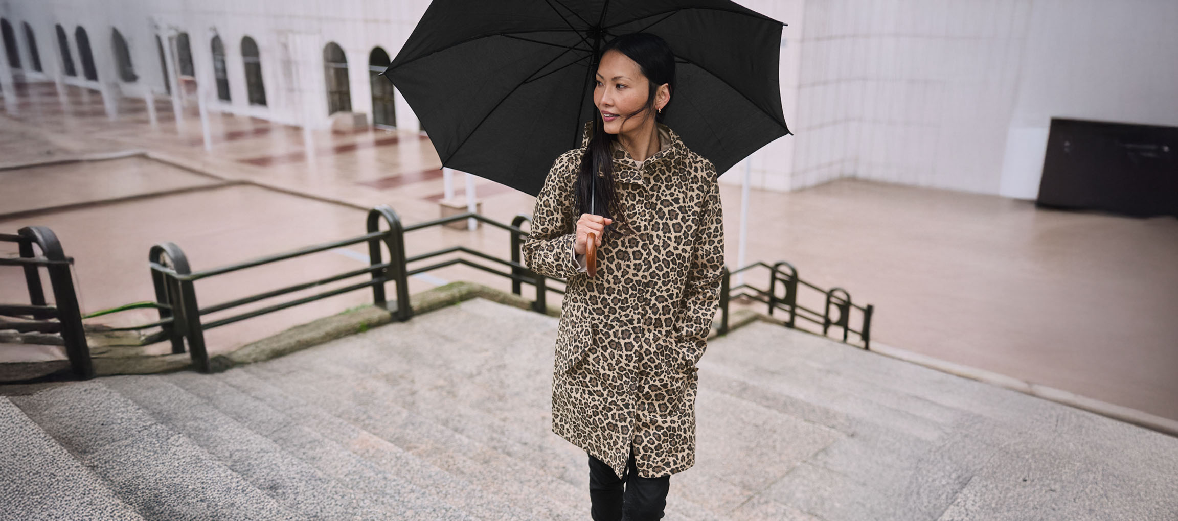 Moteris su leopardo rašto paltu ir skėčiu ant laiptų.