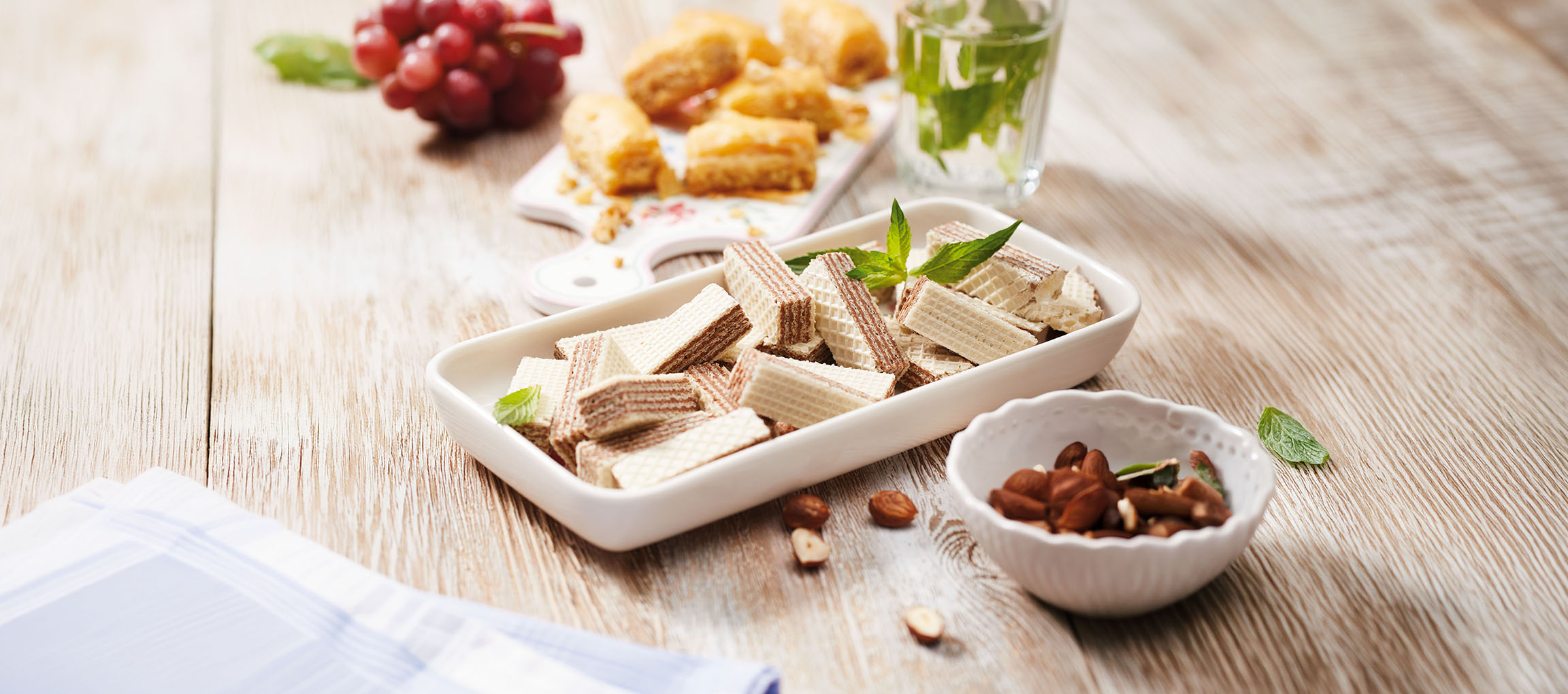 Vafliai, baklava, vynuogės ir mėtų vanduo ant medinio stalo.