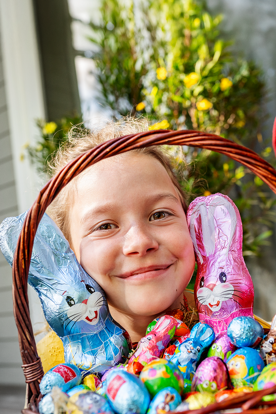 Šypsosi vaikas su velykinių šokoladinių zuikių ir kiaušinių krepšeliu.