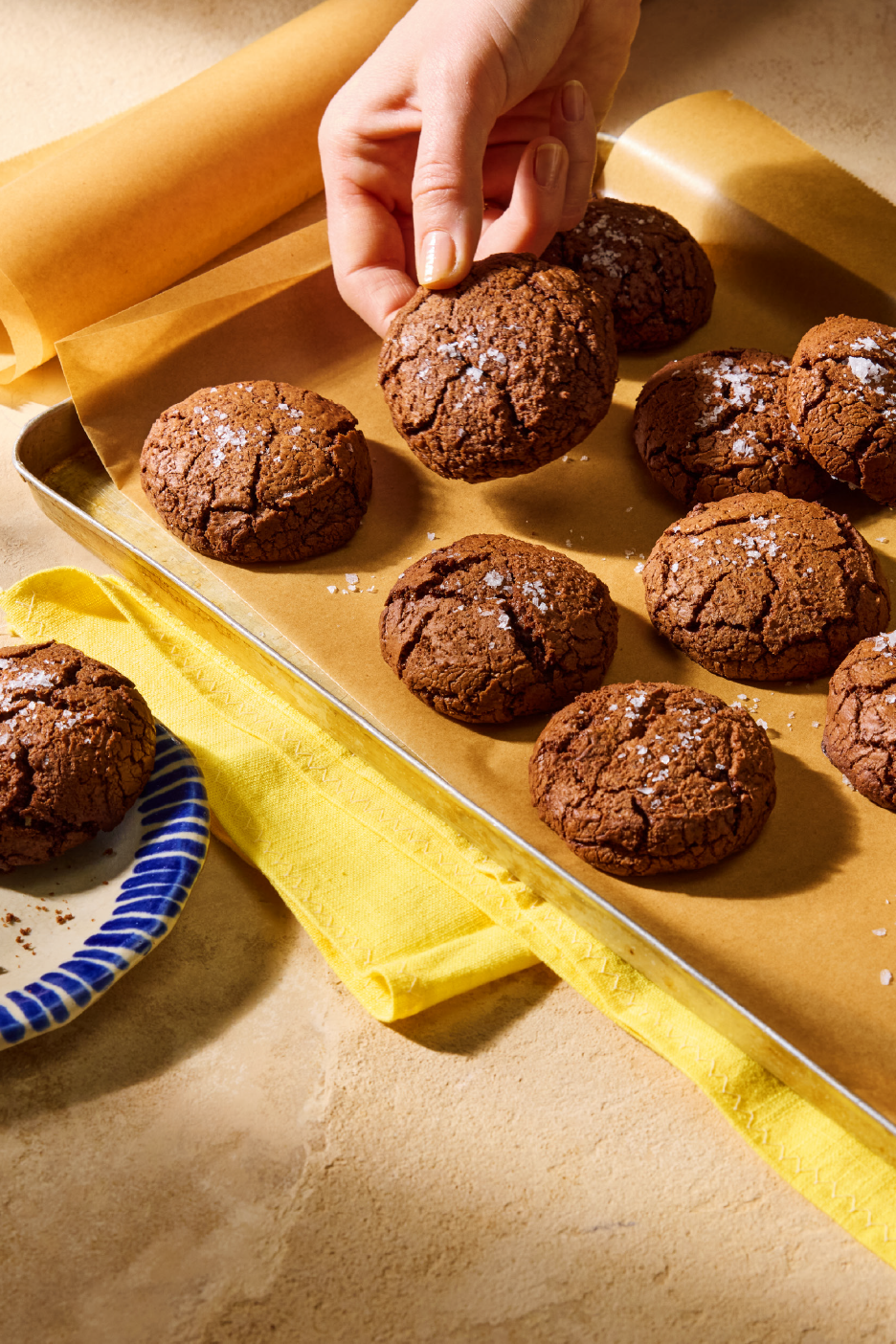 Rankos paima šokoladinį sausainį su druska nuo kepimo skardos.