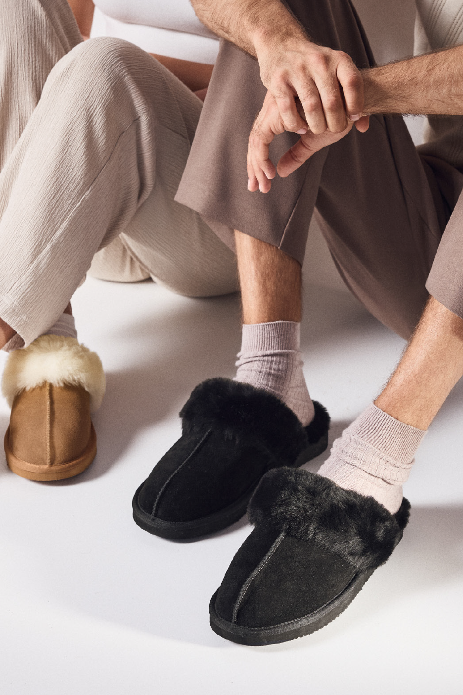 Du žmonės sėdi ant grindų, avėdami šlepetes su kailiu.