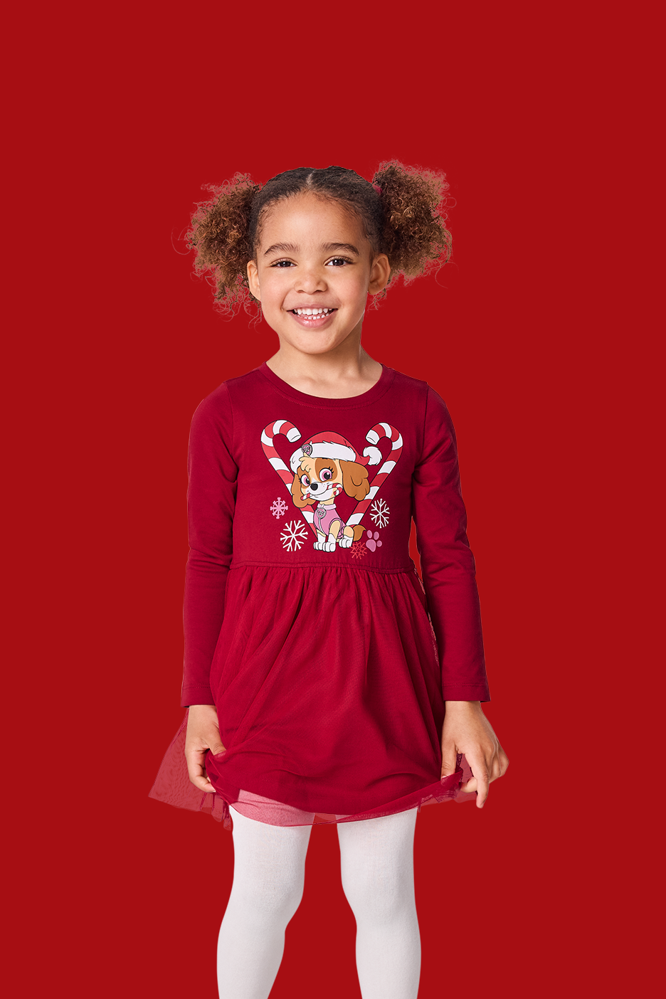 Mergaitė su raudona suknele su „Paw Patrol“ šuniuku ir baltomis pėdkelnėmis.