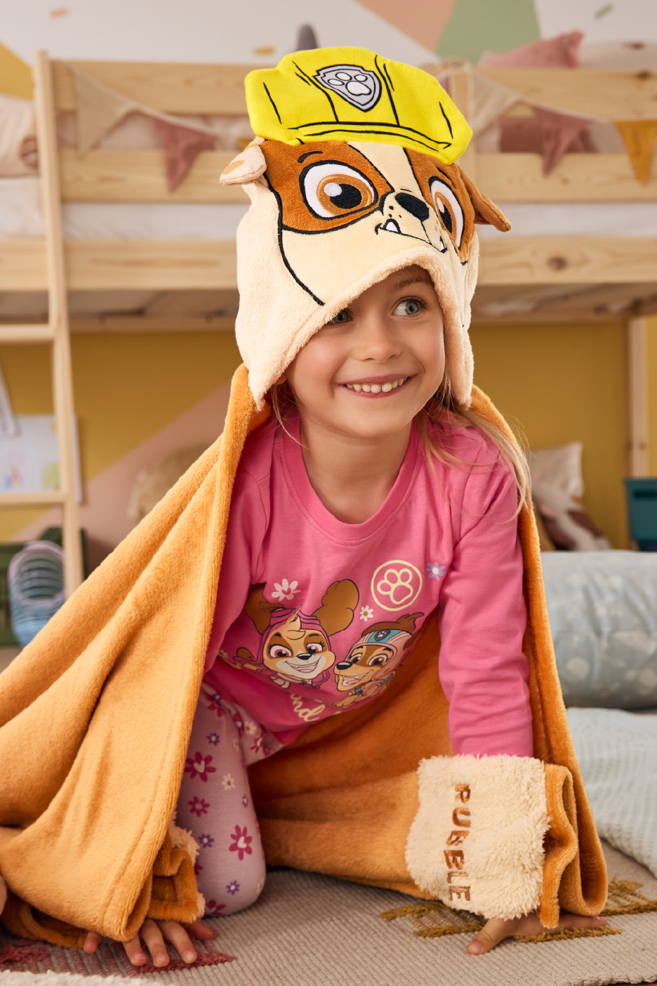 Mergaitė su „Paw Patrol“ Rubble antklode ir pižama, šypsosi.