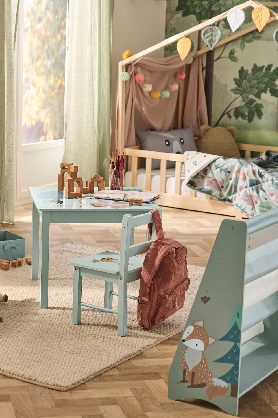 Vaikų kambarys su mediniu namelio formos lovos rėmu, žalsvu stalu ir kėde.