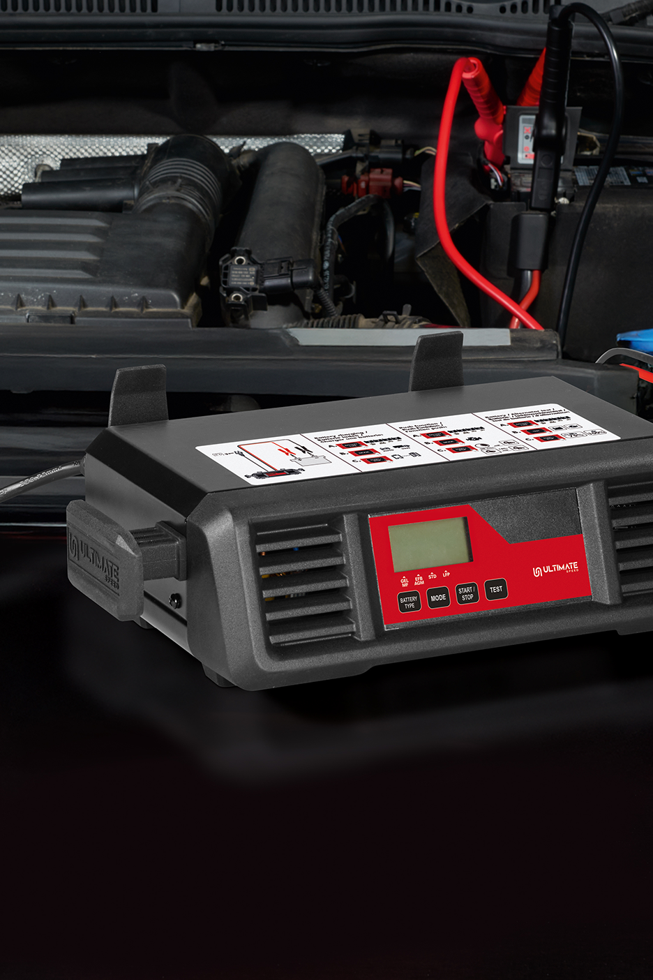 Automobilio akumuliatoriaus įkroviklis „Ultimate Speed“ su prijungtais gnybtais variklio skyriuje.
