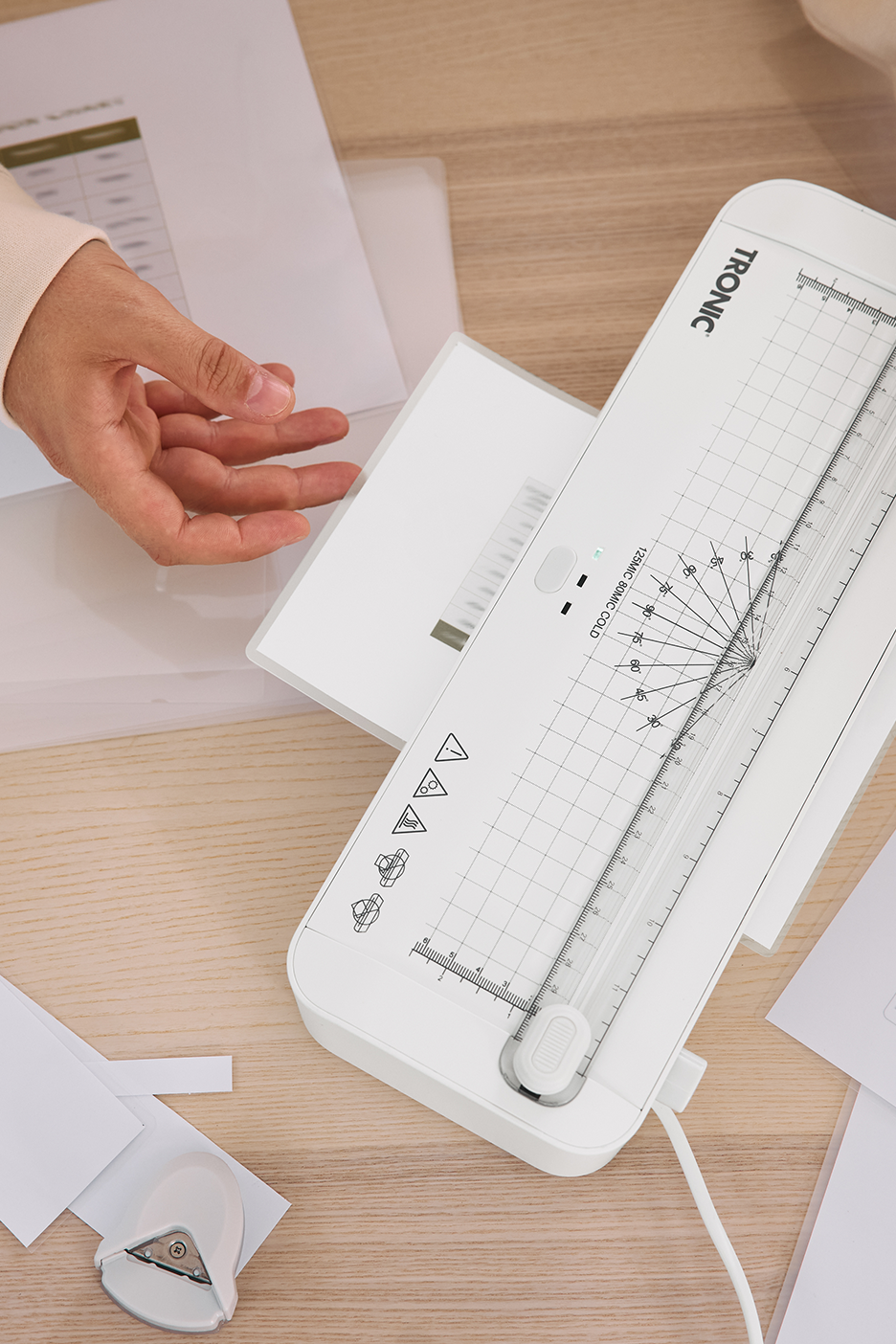 Asmuo laminuoja dokumentą baltu „Tronic“ laminatoriumi ant medinio stalo.