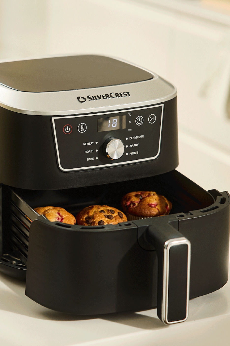 Juodas oro gruzdintuvas su skaitmeniniu ekranu, kuriame rodoma „18“, ir trimis keksiukais krepšelyje.