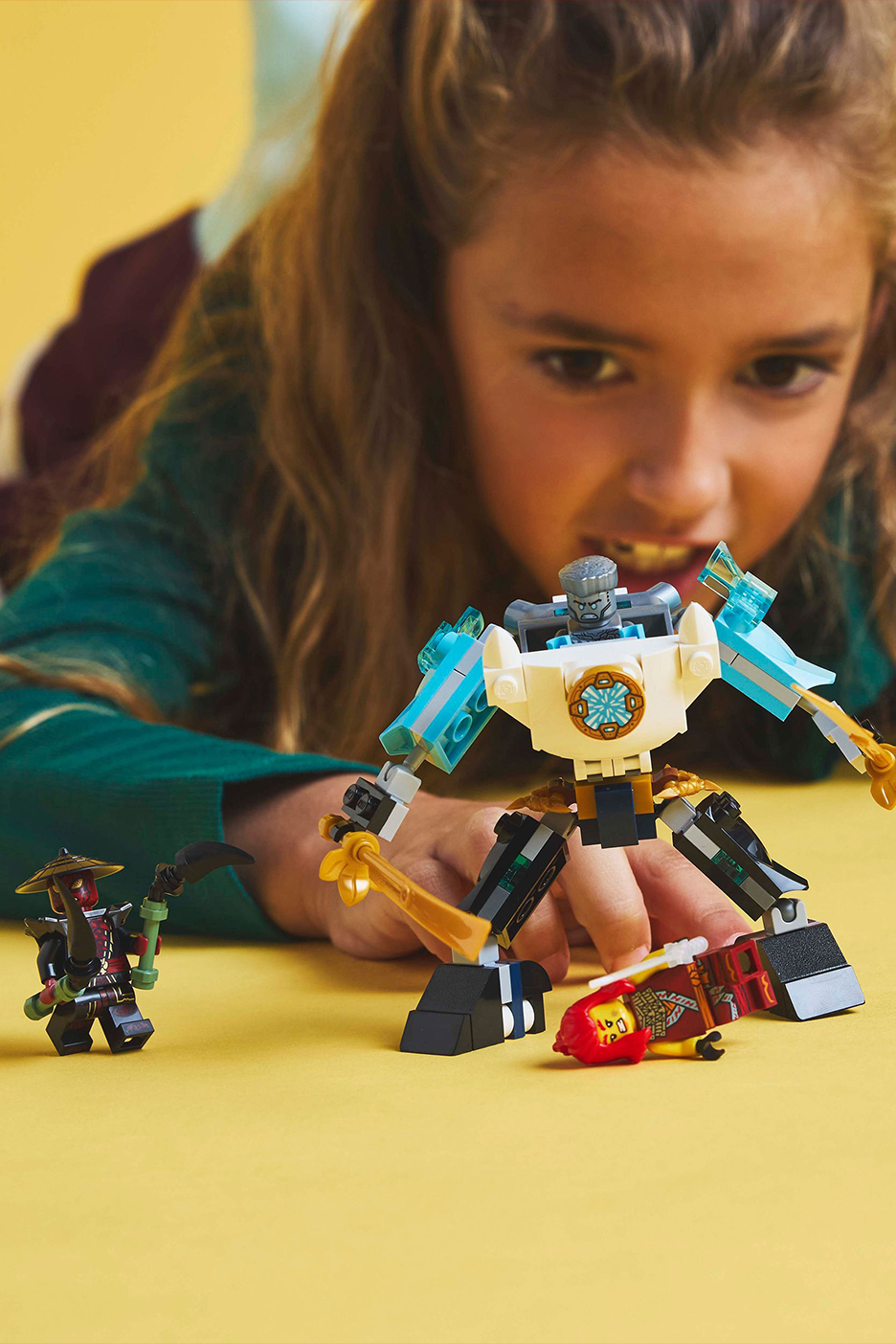 Mergaitė žaidžia su konstruojamais žaislais, įskaitant robotą ir dvi minifigūrėles.