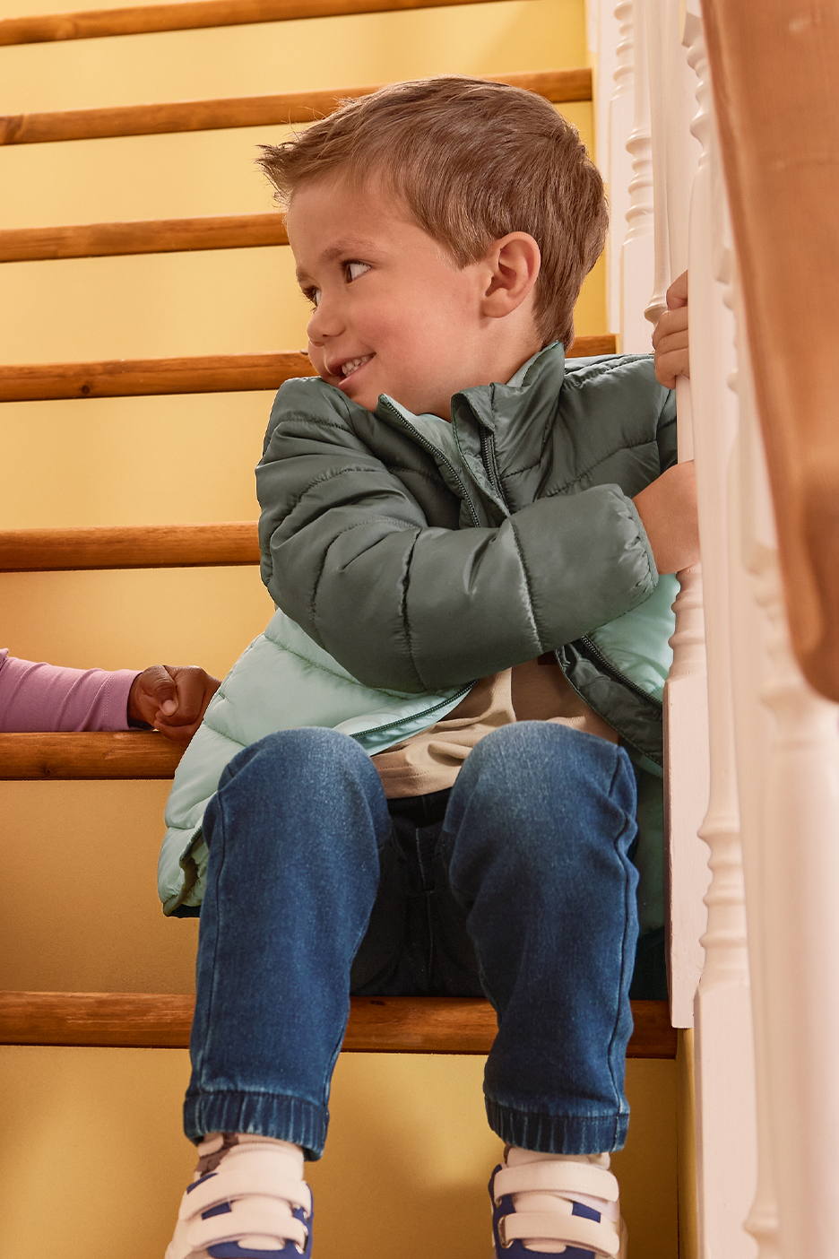 Berniukas su dygsniuota striuke ir džinsais sėdi ant laiptų.