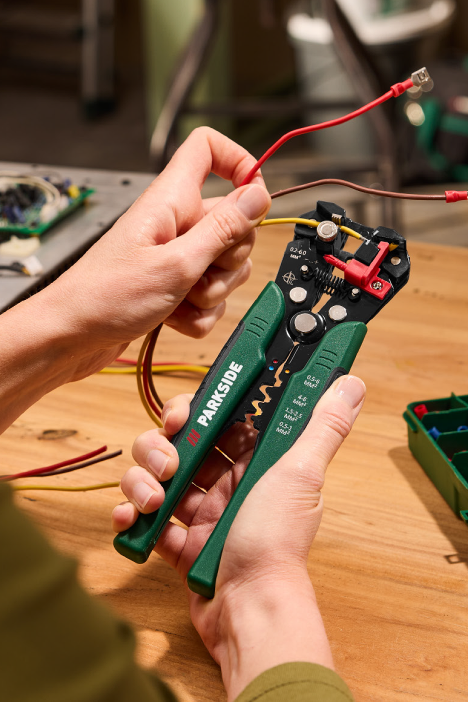 Rankos naudoja automatinį laidų nuėmiklį su laidais ant medinio stalo.