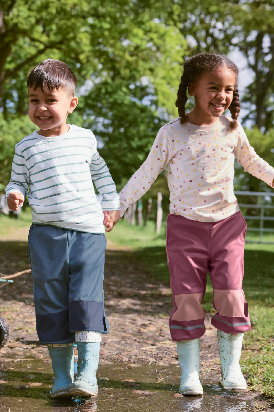 Du vaikai su neperšlampamomis kelnėmis ir guminiais batais žaidžia purvo baloje.
