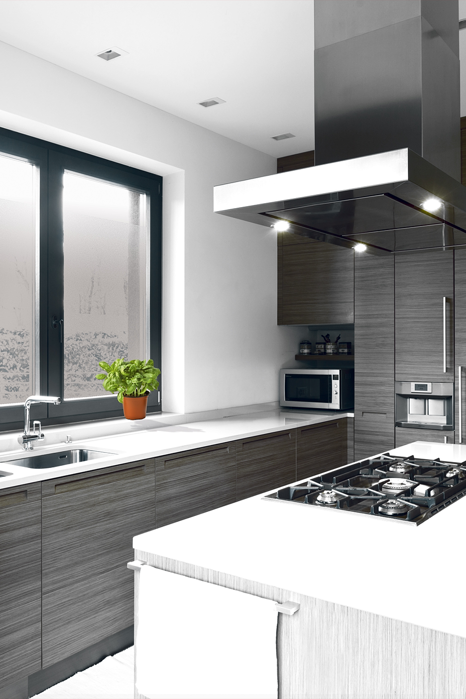 Moderni virtuvė su tamsiai pilkomis spintelėmis, baltais stalviršiais, virykle ir gartraukiu.