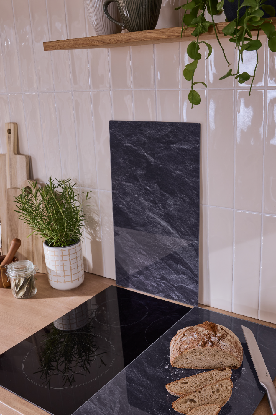 Virtuvės stalviršis su kaitlente, duona ant pjaustymo lentos ir rozmarinas vazonėlyje.