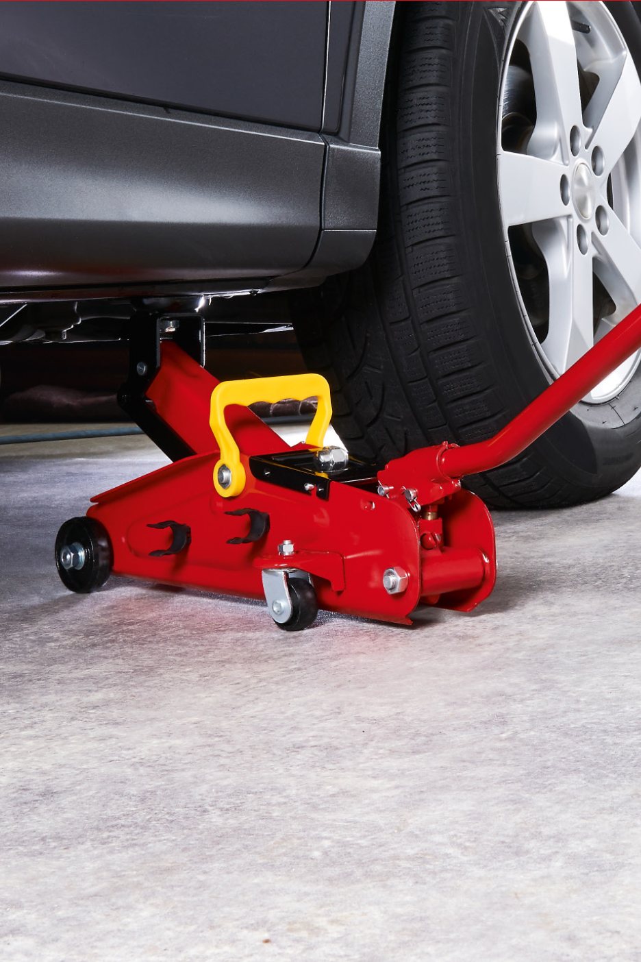 Raudonas hidraulinis domkratas po pilku automobiliu, paruoštas pakelti.