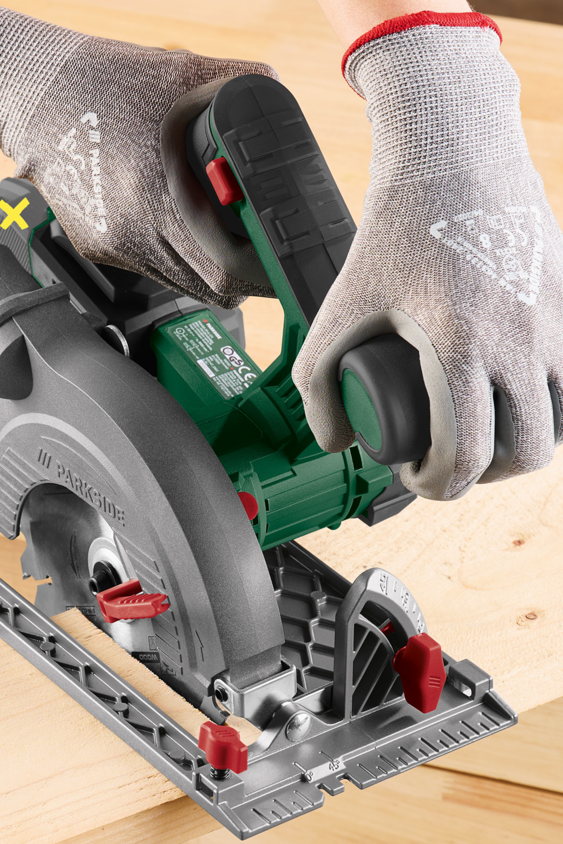 Rankinis diskinis pjūklas su apsauginėmis pirštinėmis pjauna medieną.