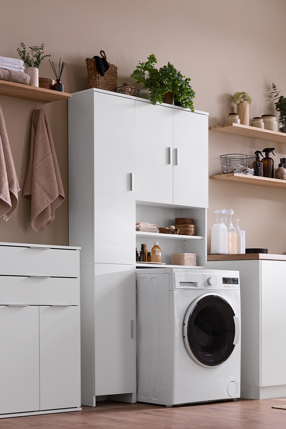 Skalbykla su baltais baldais, skalbimo mašina, lentynomis ir augalais.