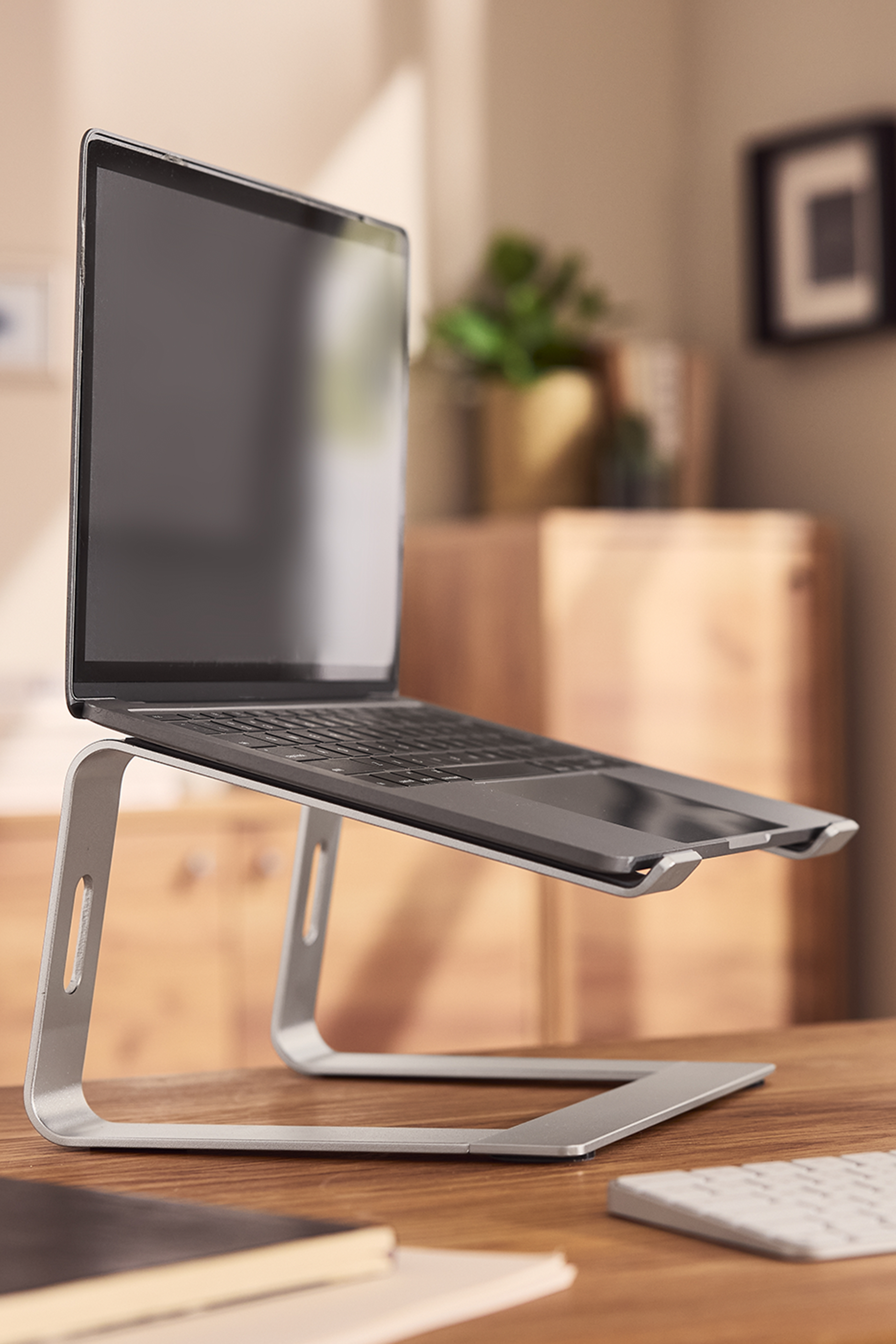 Nešiojamasis kompiuteris ant sidabrinio stovo ant medinio stalo.