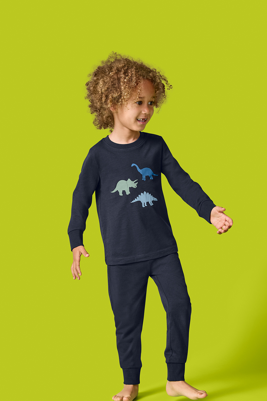 Berniukas su tamsiai mėlyna pižama su dinozaurų atspaudais.