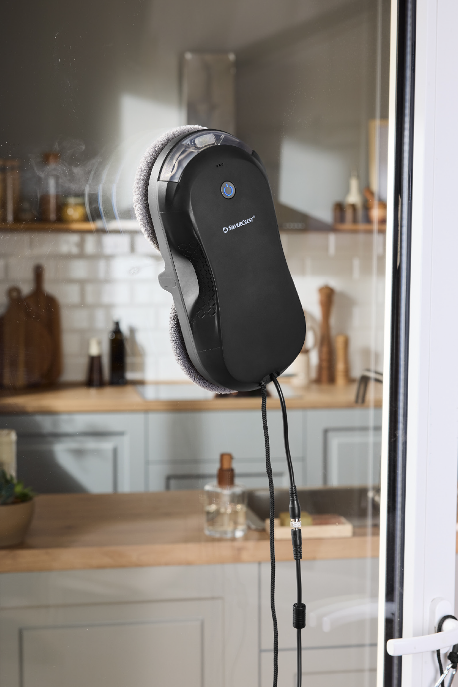 Robotas langų valytuvas valo langą virtuvės fone.