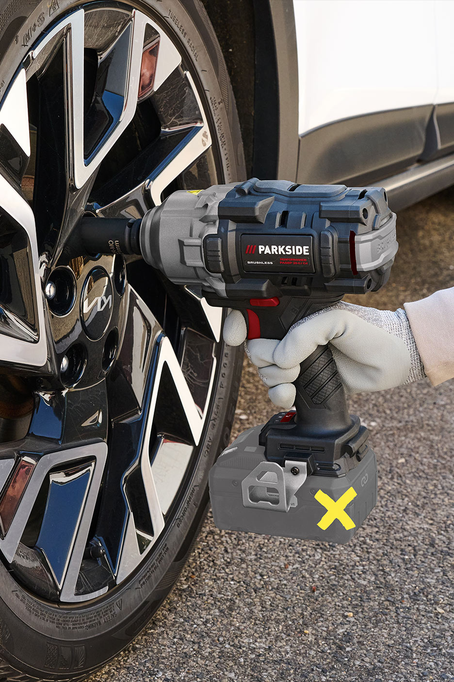 Asmuo, mūvintis pirštines, naudoja akumuliatorinį smūginį veržliasukį automobilio ratui.