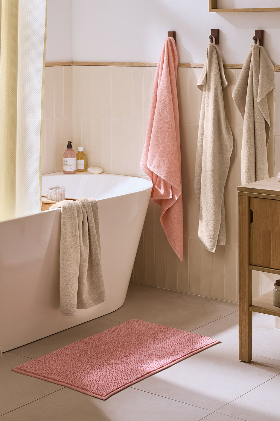 Vonios kambarys su rožiniu kilimėliu, vonia ir rankšluosčiais.