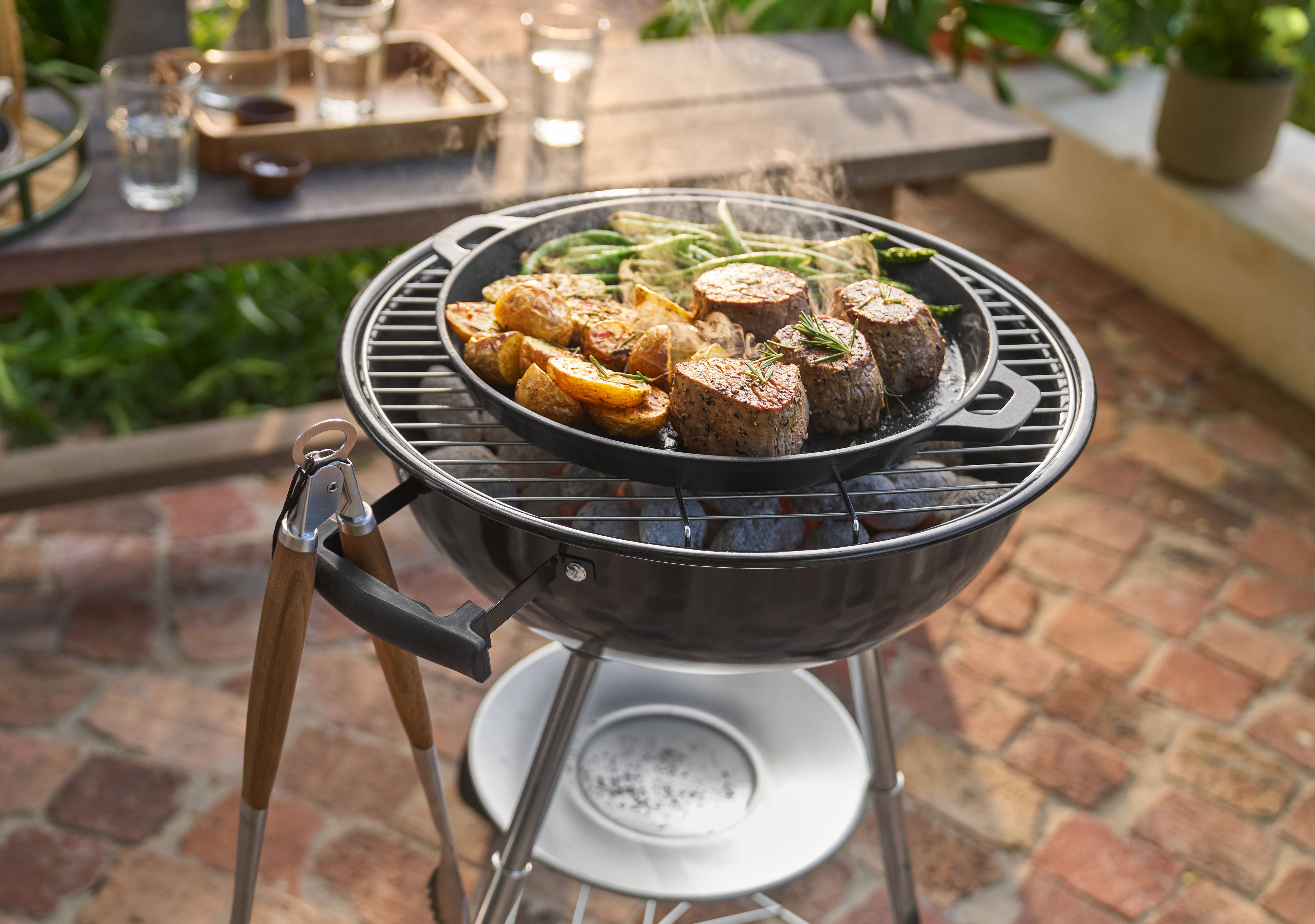 Kepsninė su mėsa, bulvėmis ir žaliomis pupelėmis, kepančiomis keptuvėje lauke.