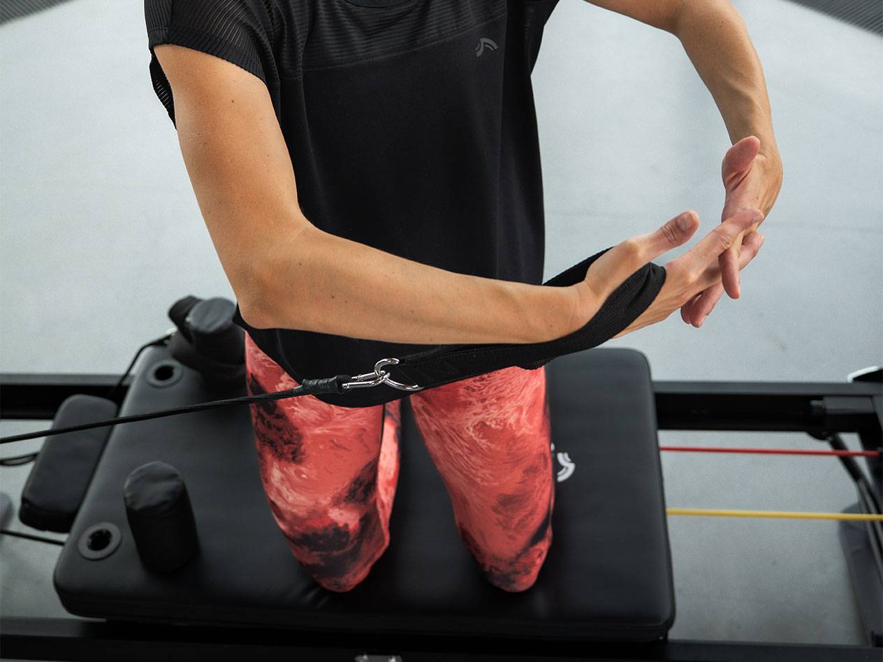 Moteris sportuoja su pasipriešinimo juostomis ant Pilates treniruoklio.