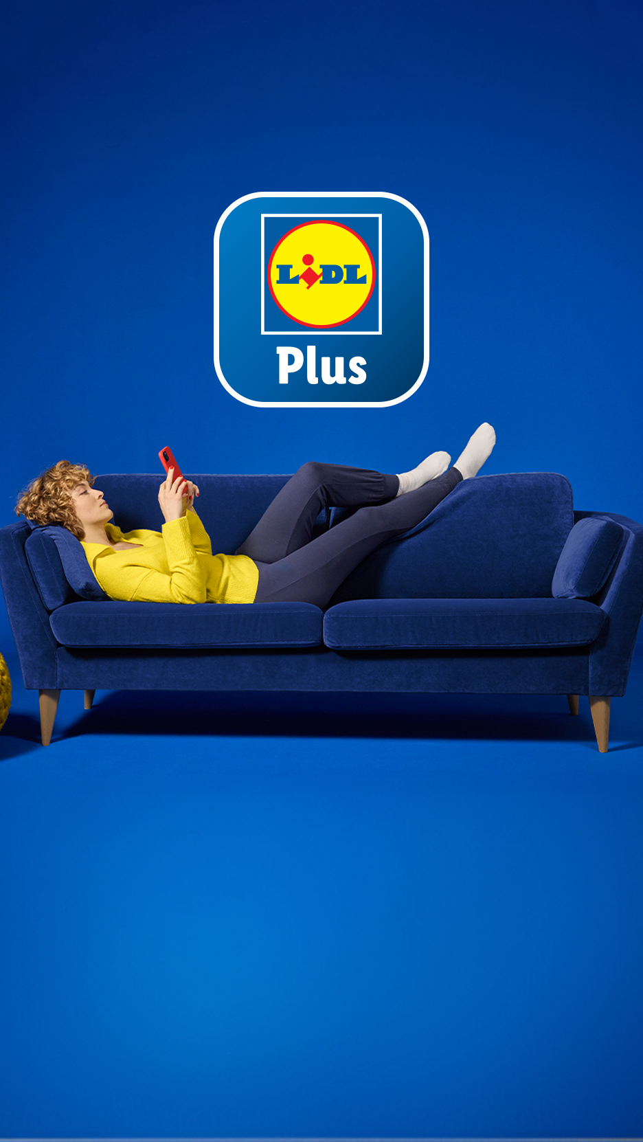 Moteris guli ant mėlynos sofos ir naudojasi telefonu, virš jos – „Lidl Plus“ programėlės logotipas.