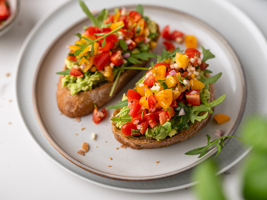 Avokadų skrebučiai su pomidorais ir raudonaisiais svogūnais ant pilkos lėkštės.