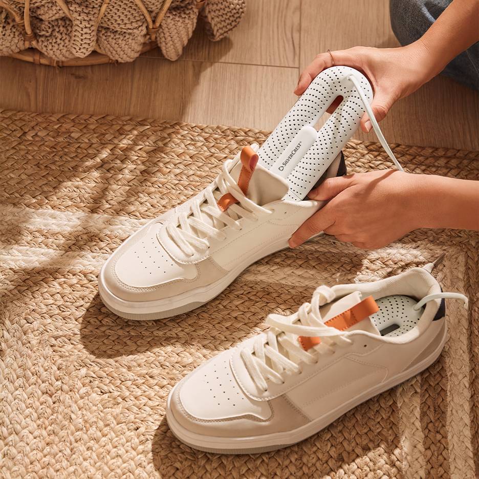 Silvercrest batų džiovintuvas baltuose sportbačiuose ant pintos kilimėlio.