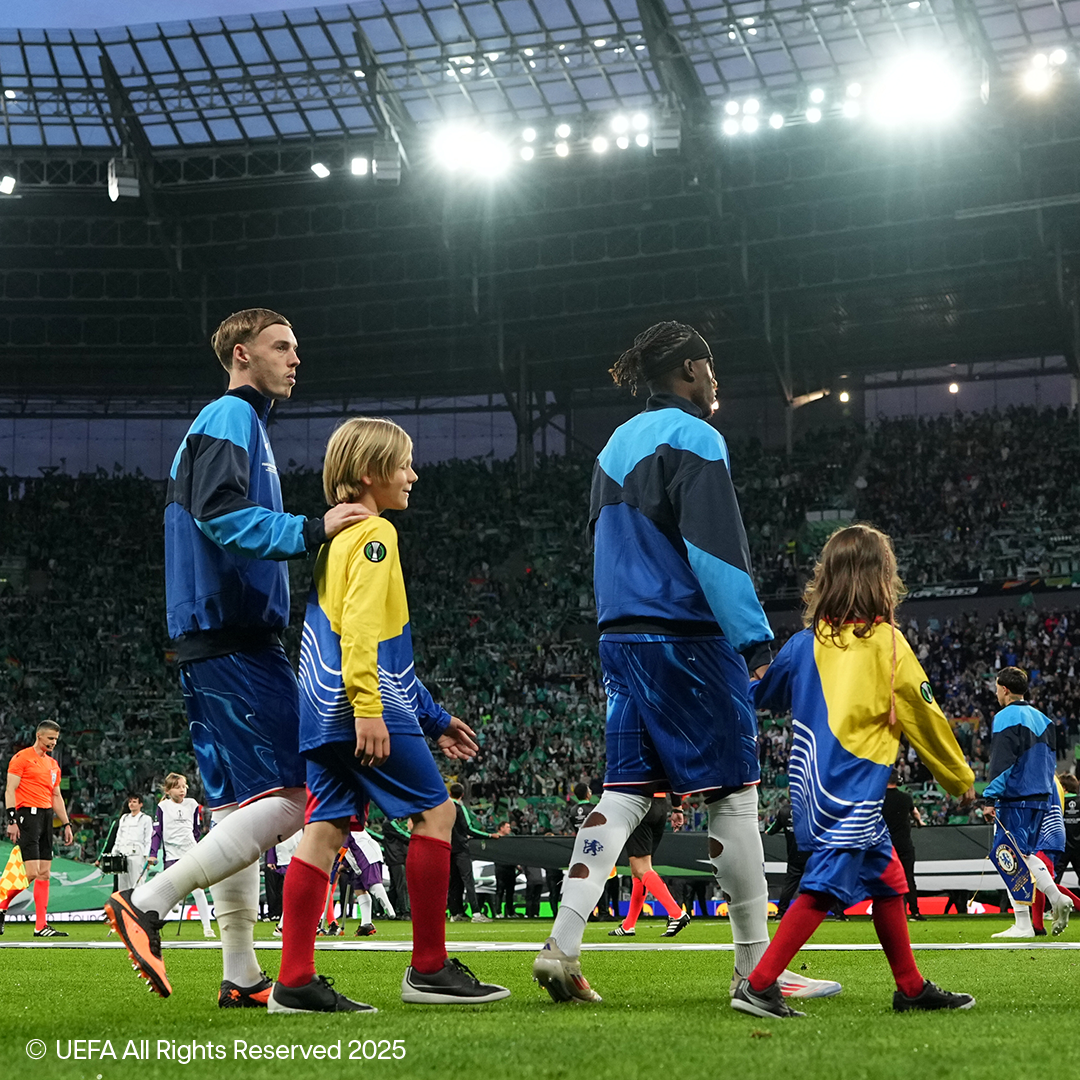 Futbolininkai ir vaikai eina pilno stadiono aikšte.