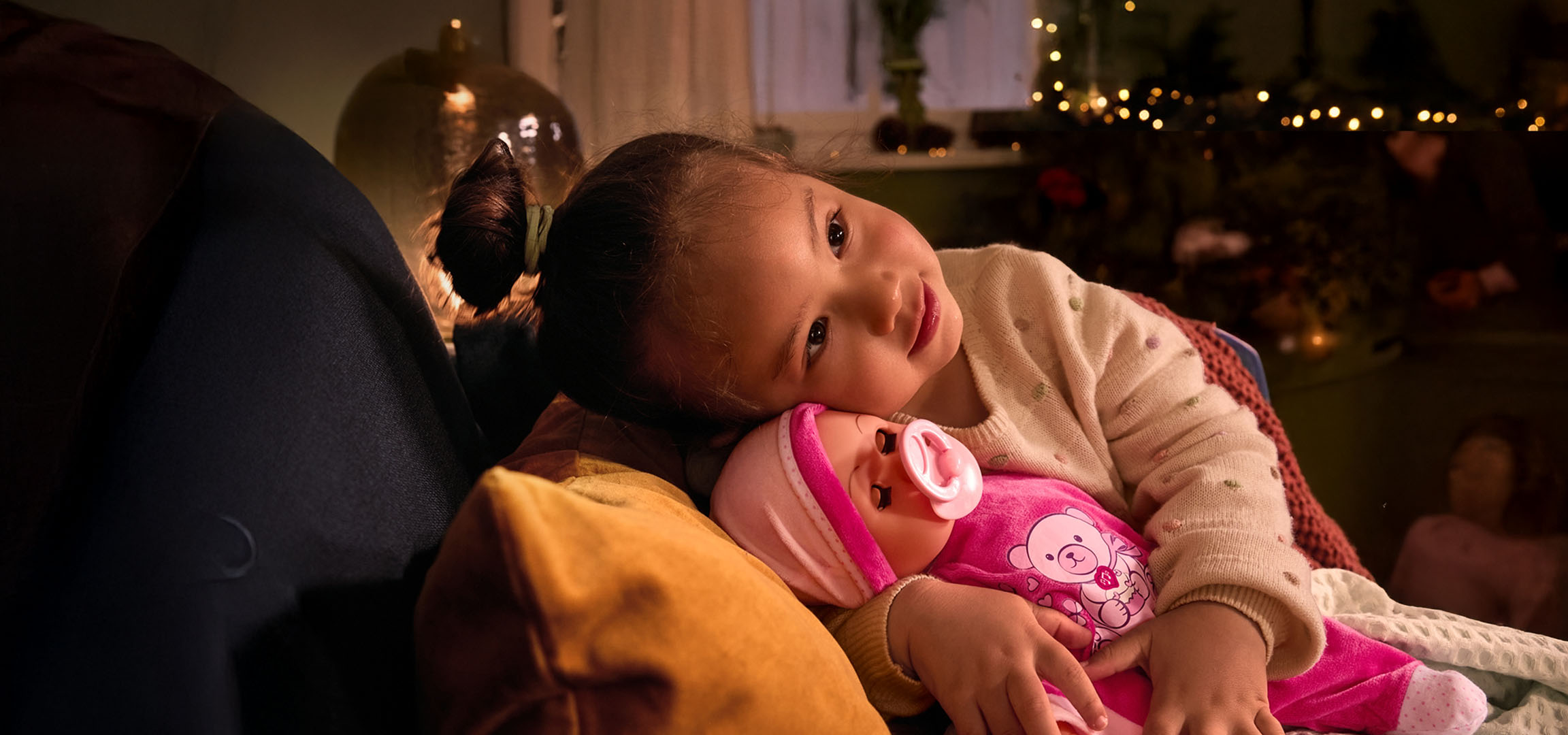 Mergaitė su lėle ir čiulptuku, jaukiai įsitaisiusi ant pagalvės.