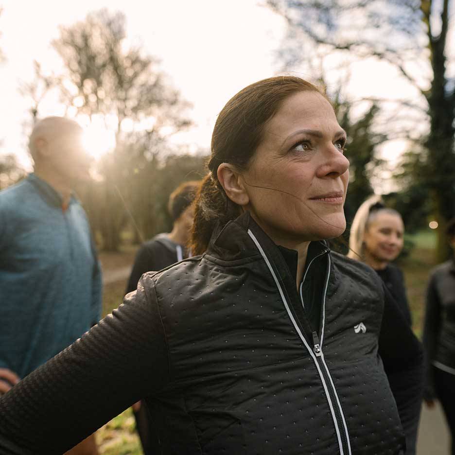 Moteris su juoda sportine striuke žiūri aukštyn, fone – žmonių grupė.