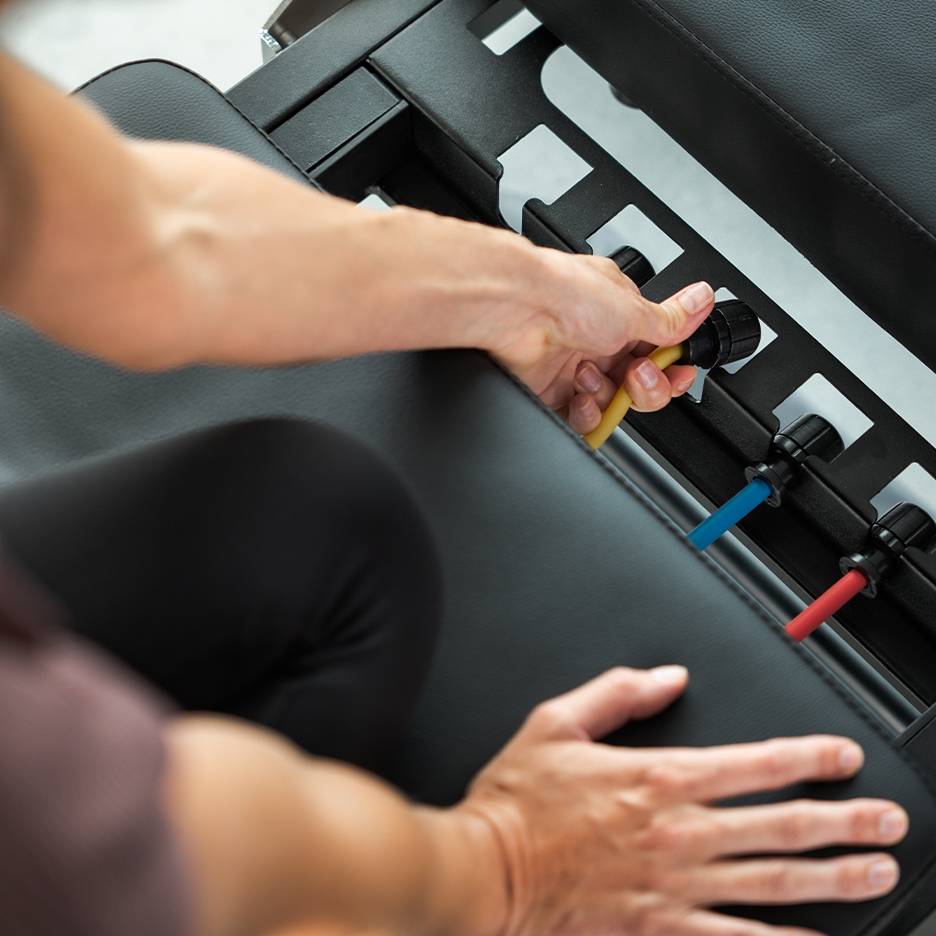 Asmuo reguliuoja pasipriešinimo juostas ant treniruočių suoliuko.