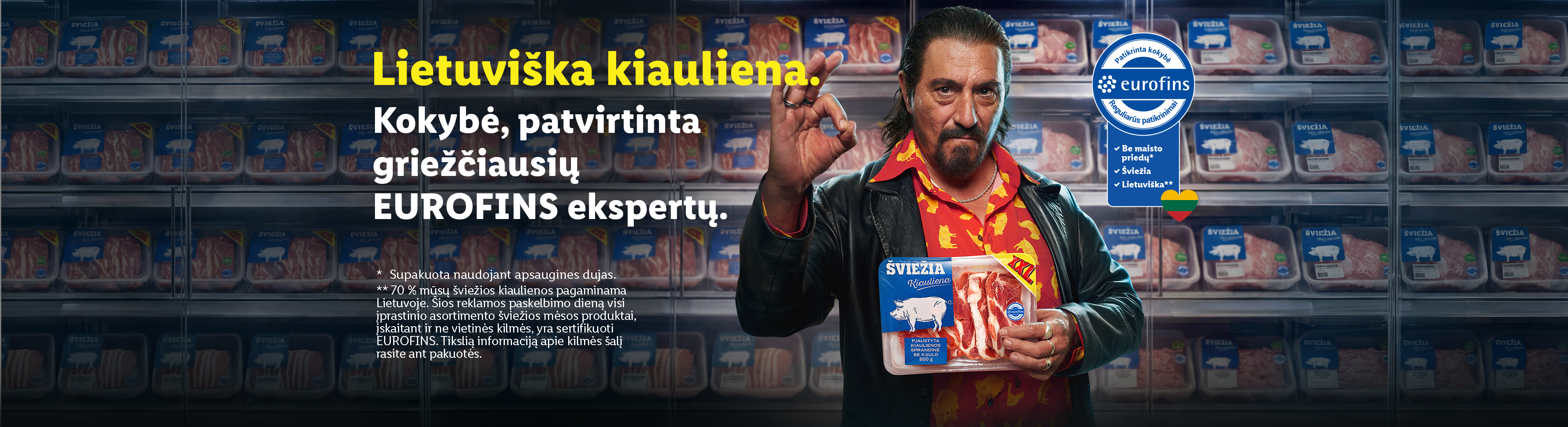 Vyras su šviežios kiaulienos pakuote, apsuptas šaldytuvo su mėsos produktais, reklamuojantis lietuvišką kiaulieną.