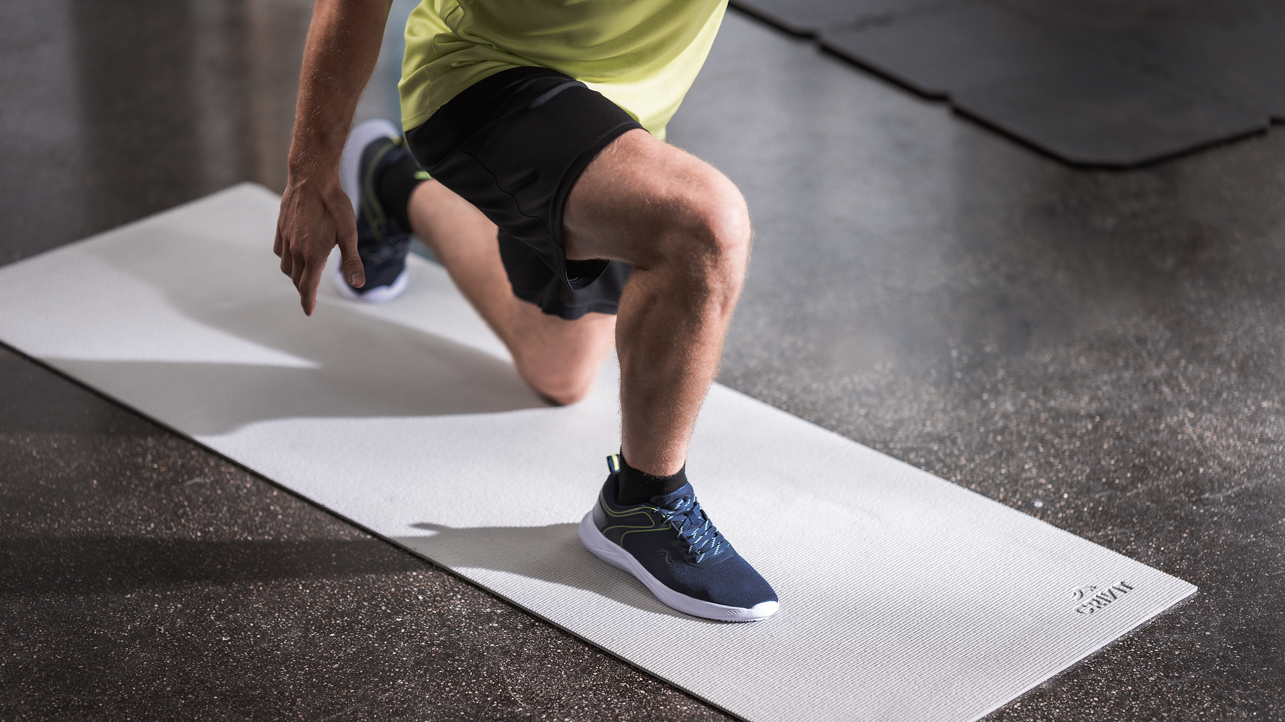 Vyras sportine apranga daro įtūpstus ant šviesiai pilko mankštos kilimėlio.