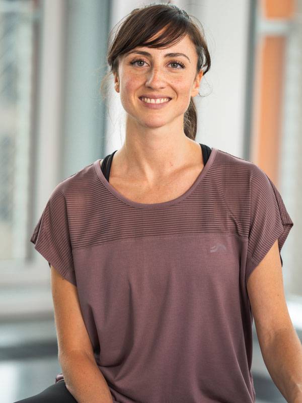 Besišypsanti moteris, dėvinti violetinius sportinius marškinėlius trumpomis rankovėmis.