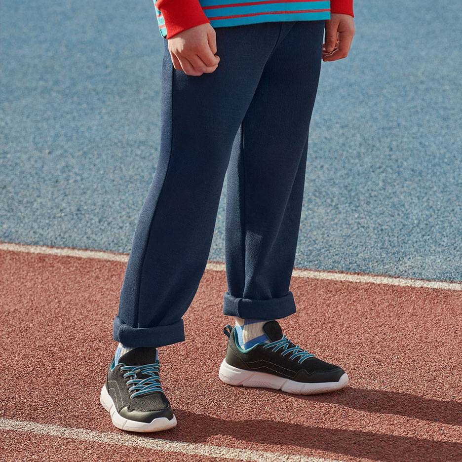 Tamsiai mėlynos sportinės kelnės ir juodi sportbačiai su mėlynais raišteliais ant bėgimo takelio.