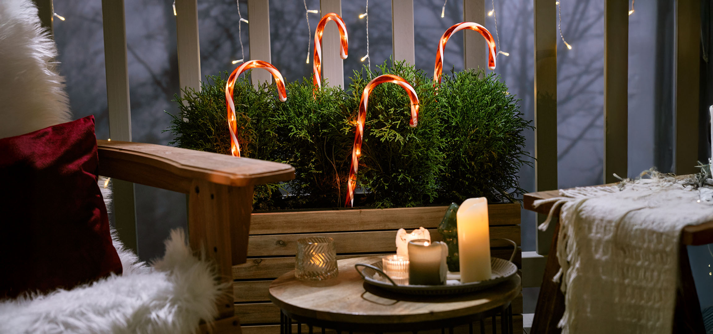 Kalėdoms papuoštas balkonas su kėde, žvakėmis ir saldainių lazdelėmis.