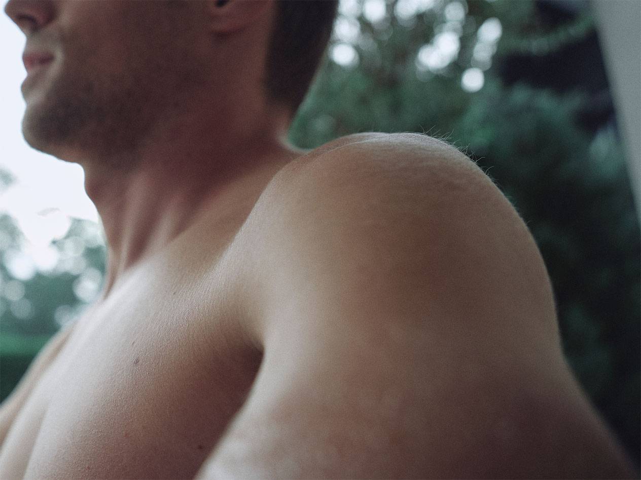 Stambus vyro peties ir kaklo planas, su neryškiu žaliu fonu.