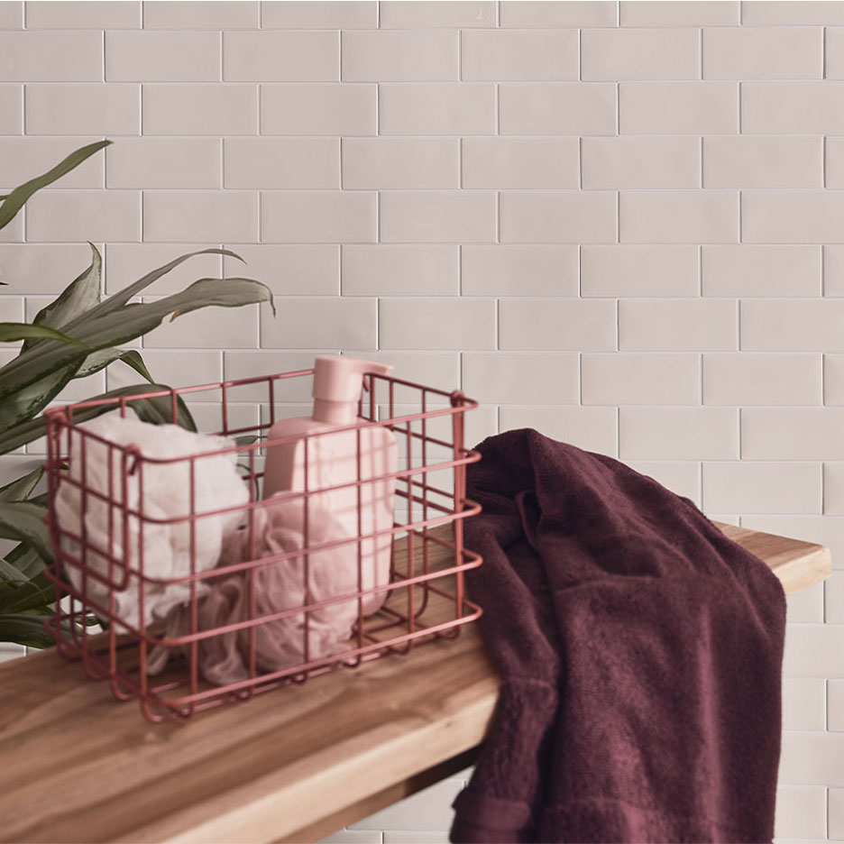 Vonios kambario dekoras su baltomis plytelėmis, mediniu suoliuku, krepšeliu su muilu ir rankšluosčiais.