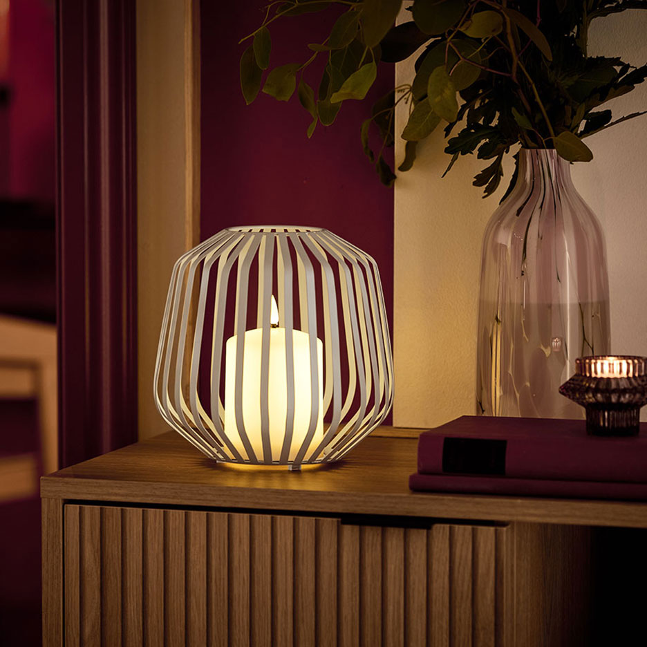 LED žvakė baltame metaliniame laikiklyje ant medinės komodos.