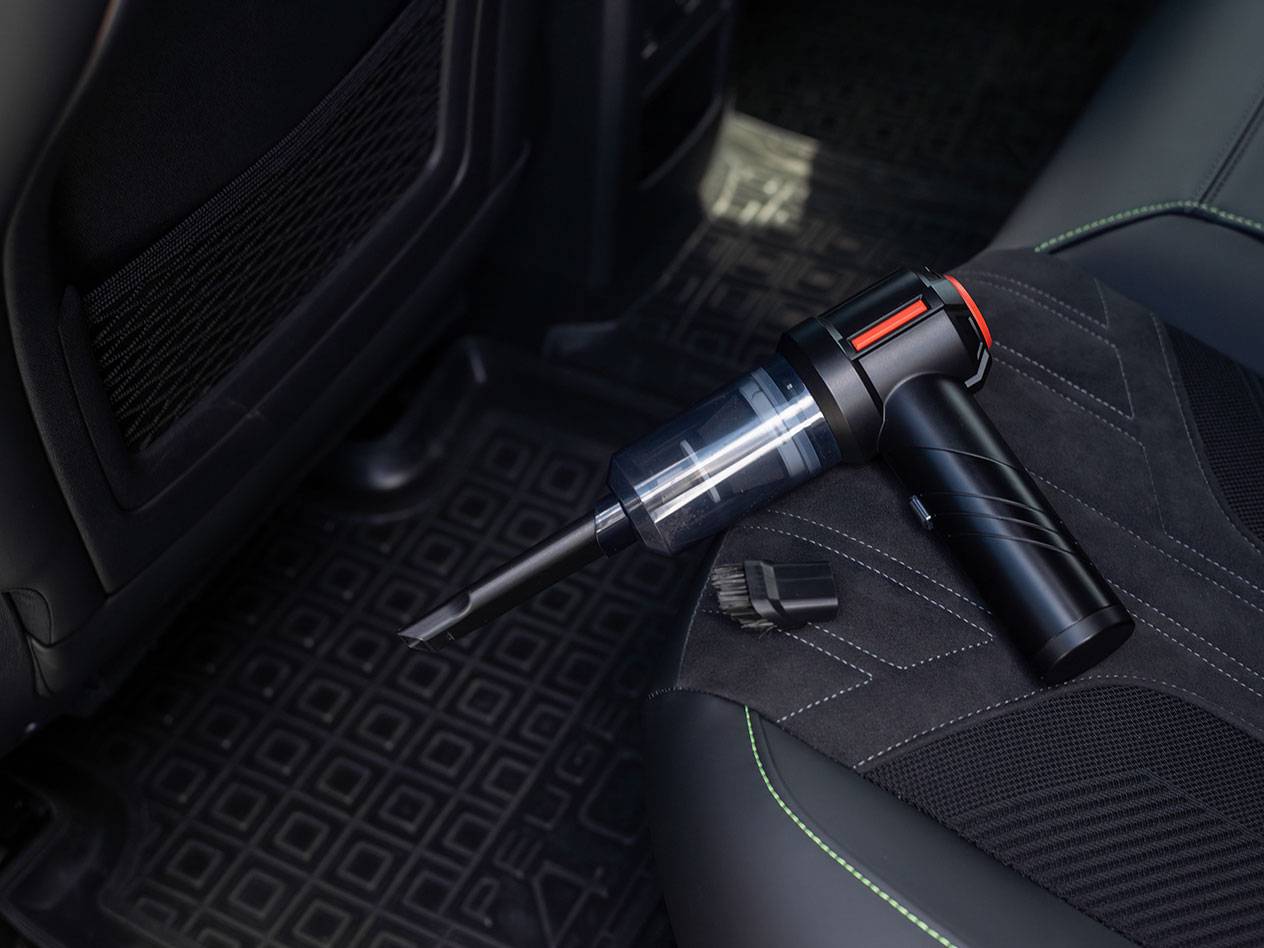Kompaktiškas rankinis dulkių siurblys su priedais ant automobilio sėdynės.