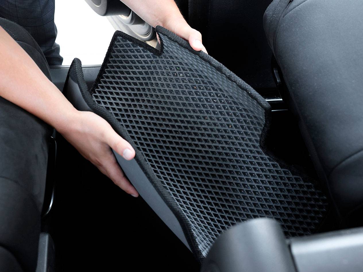 Asmuo deda juodą guminį automobilio kilimėlį su deimantiniu raštu į transporto priemonę.