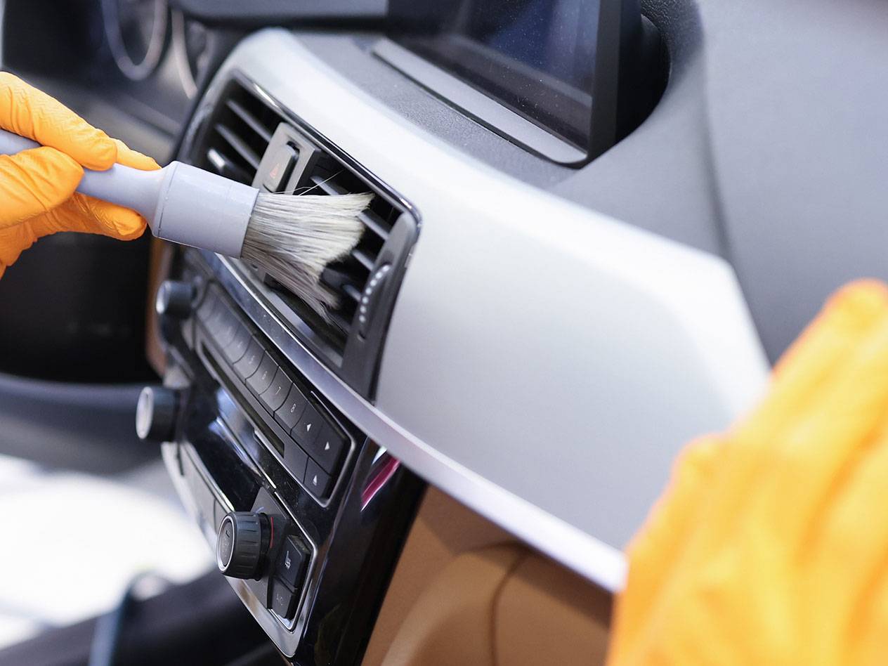 Automobilio salono valymas detalių šepetėliu ir guminėmis pirštinėmis.