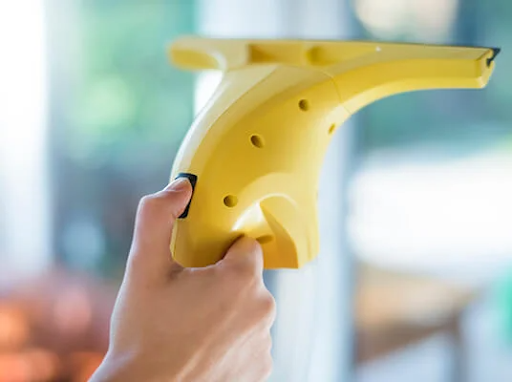 Ranka laiko geltoną elektrinį langų valytuvą, valantį langą.