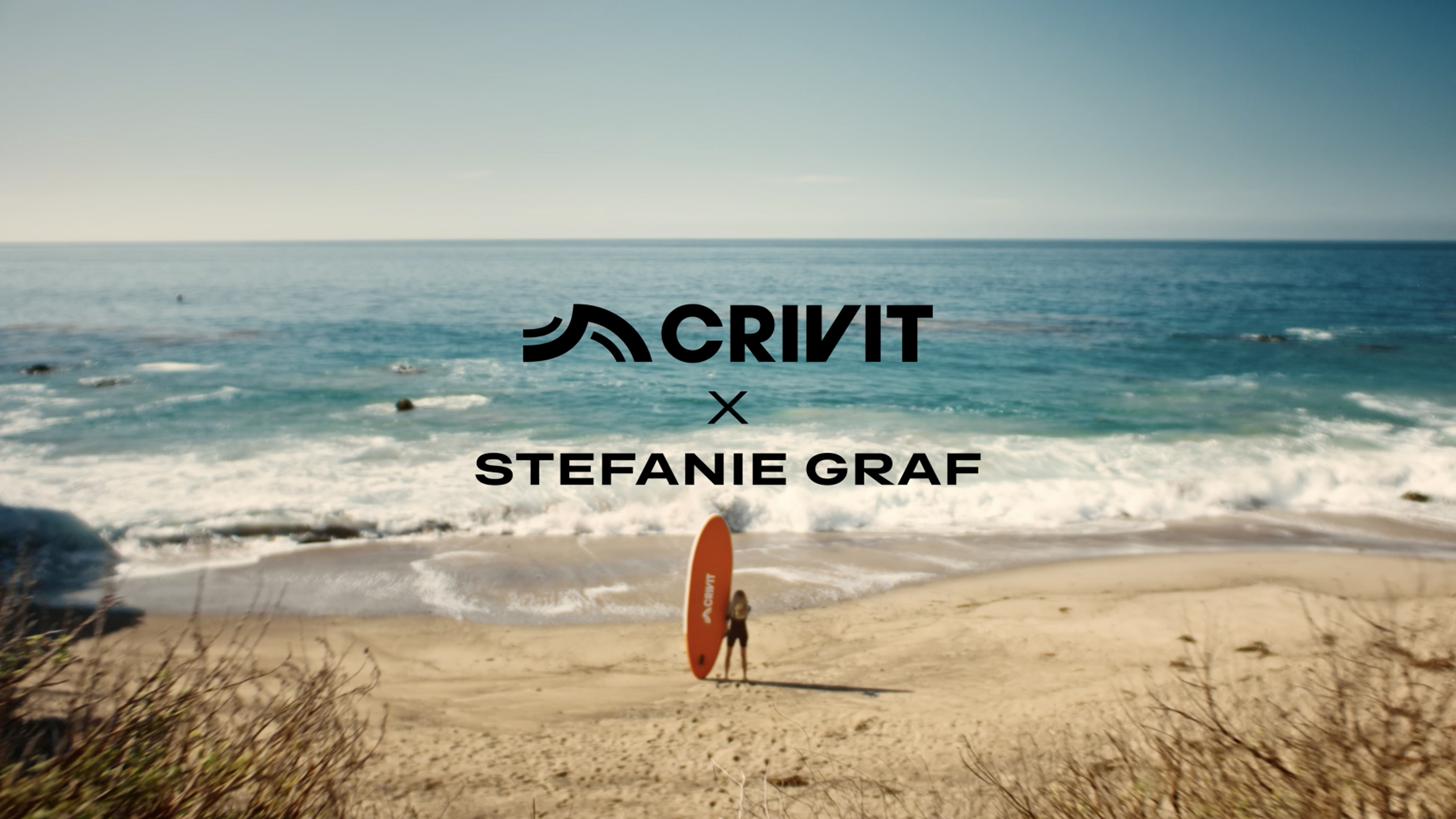 Moteris su oranžine SUP lenta smėlėtame paplūdimyje, fone – jūra.