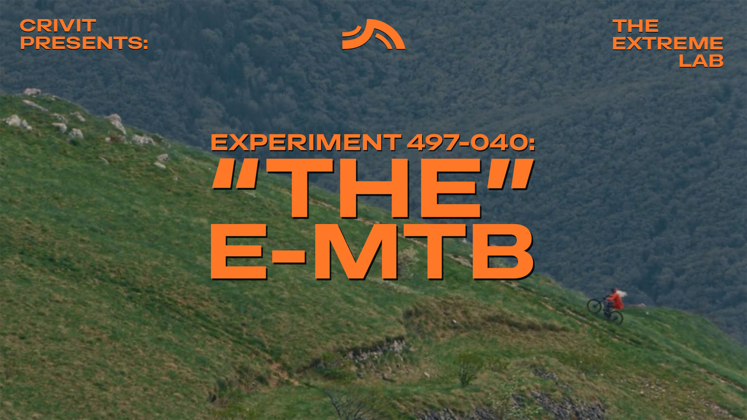 Kalnų dviratininkas ant žolėto šlaito, su tekstu 'THE E-MTB' ir 'THE EXTREME LAB'.
